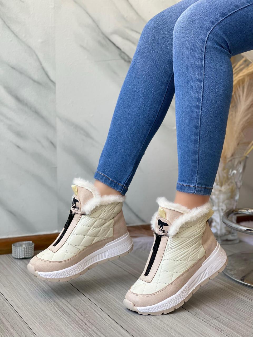 Botines blancos con detalles beige y peluche, usados con jeans azules sobre suelo de madera.