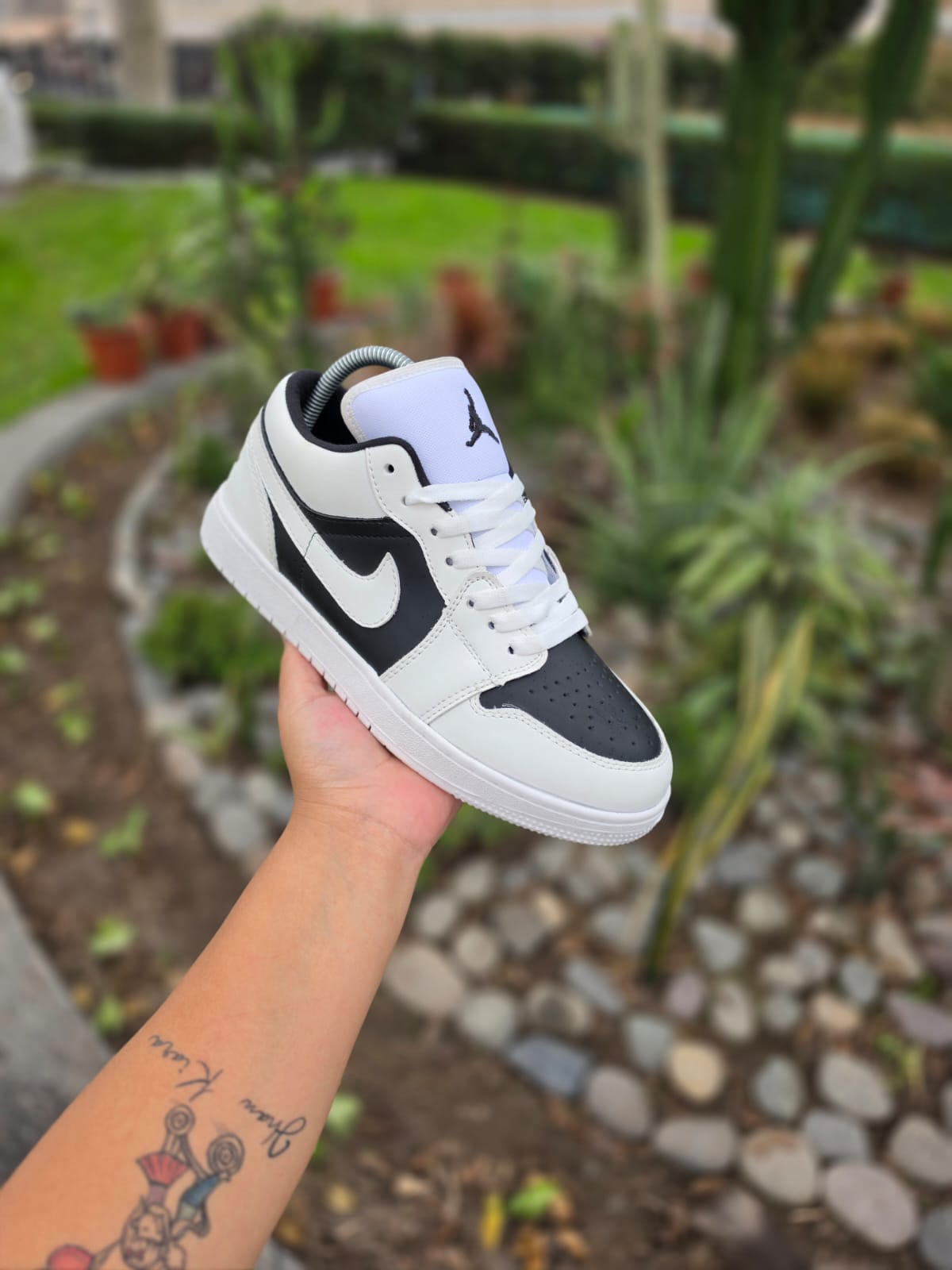 Zapatilla blanca y negra con cordones, sostenida en mano, fondo jardín desenfocado con plantas.